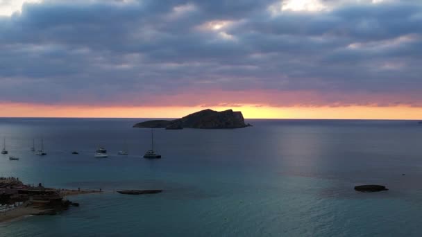 イビサのボートと素晴らしい日没の空を伴うビーチの空中ビュー 静的な三脚ホバリングドローン — ストック動画