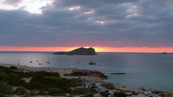 イビサのボートと素晴らしい日没の空を伴うビーチの空中ビュー アセンデッド ドローン ストック動画