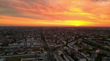 Panorama yörüngesinde insansız hava aracı. Gündoğumunda uyanan şehir, canlı turuncu gökyüzü olarak sakin şehir manzarası. Sabahın erken saatlerinde çevre ışığı