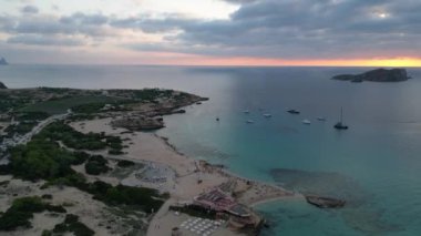 Ibiza 'da tekneli Cala Comte plajı ve çarpıcı bir günbatımı manzarası. panorama genel görünüm dronu 