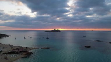 Ibiza 'da tekneli Cala Comte plajı ve çarpıcı bir günbatımı manzarası. panorama genel görünüm dronu 