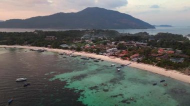 İHA. Muhteşem bir Tayland plajının üzerinde güneş batıyor, turistler manzaranın tadını çıkarıyor. Turuncu ve altın rengi gökyüzü okyanusa sıcak bir ışık saçıyor. Yaz tatili için mükemmel bir yer. panorama genel görünüm dronu 