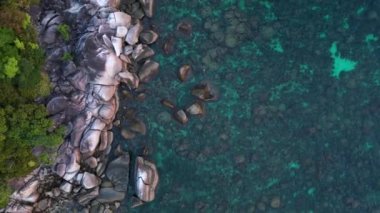 Tropikal bir adanın, turkuaz suların ve kayalık kıyı şeridinin güzelliğini yakalayan bu hava manzarası engebeli kayalıklara ve kıyılara karşı canlı mavi ve yeşil renkler gösteriyor. Yukarıdan insansız hava aracı görüntüleri 