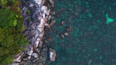 Tropikal bir adanın, turkuaz suların ve kayalık kıyı şeridinin güzelliğini yakalayan bu hava manzarası engebeli kayalıklara ve kıyılara karşı canlı mavi ve yeşil renkler gösteriyor. Yukarıdan insansız hava aracı görüntüleri 