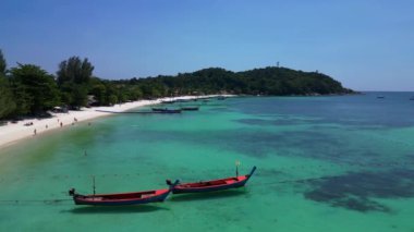 Turistler, turkuaz suya demirlemiş geleneksel Tayland uzun kuyruklu tekneleriyle tropikal bir adada güneşli bir günün tadını çıkarıyorlar. doly sağ drone 