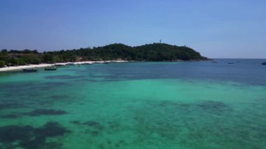 Turistler, turkuaz suya demirlemiş geleneksel Tayland uzun kuyruklu tekneleriyle tropikal bir adada güneşli bir günün tadını çıkarıyorlar. Dolly sol İHA 