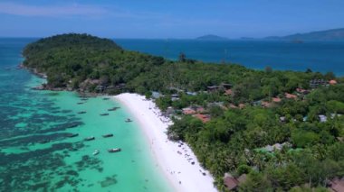 Turistler, turkuaz suya demirlemiş geleneksel Tayland uzun kuyruklu tekneleriyle tropikal bir adada güneşli bir günün tadını çıkarıyorlar. panorama genel görünüm dronu 