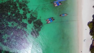 Turistler, turkuaz suya demirlemiş geleneksel Tayland uzun kuyruklu tekneleriyle tropikal bir adada güneşli bir günün tadını çıkarıyorlar. Yukarıdan insansız hava aracı görüntüleri 