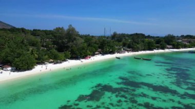 Turistler, turkuaz suya demirlemiş geleneksel Tayland uzun kuyruklu tekneleriyle tropikal bir adada güneşli bir günün tadını çıkarıyorlar. panorama yörünge dronu 
