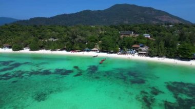 Turistler, turkuaz suya demirlemiş geleneksel Tayland uzun kuyruklu tekneleriyle tropikal bir adada güneşli bir günün tadını çıkarıyorlar. geniş yörünge görünümü dronu 