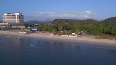 Sol İHA 'ya dön. Langkawi sahil şeridinin havadan görünüşü, turistlerin berrak mavi suların tadını çıkardığı tropik bir plajdaki otel ve tatil beldelerini gösteriyor.