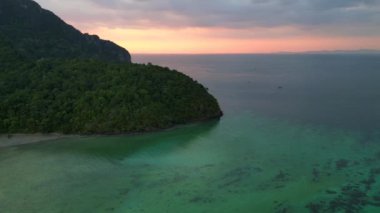 Panorama yörünge dronu. Günbatımında, turkuaz bir denizde yelken açan teknelerle tropikal bir adanın havadan görünüşü.