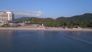 Dolly sağ drone. Turistler gün batımında kumsalda yürürken arka planda yemyeşil bir tropikal orman görüyorlar.