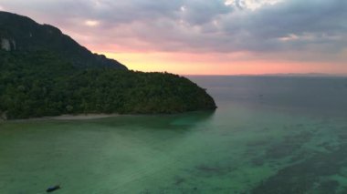 Panorama insansız hava aracı. Günbatımında, turkuaz bir denizde yelken açan teknelerle tropikal bir adanın havadan görünüşü.