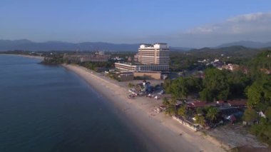 Üstten kumandalı hava aracı. Langkawi sahil şeridinin havadan görünüşü, turistlerin berrak mavi suların tadını çıkardığı tropik bir plajdaki otel ve tatil beldelerini gösteriyor.