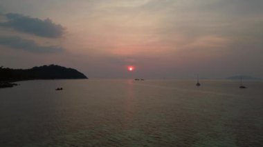 Panorama insansız hava aracı. Günbatımında geleneksel uzun kuyruklu teknelerin bulunduğu tropikal bir sahil manzarası huzurlu ve resimli bir atmosfer yaratıyor.