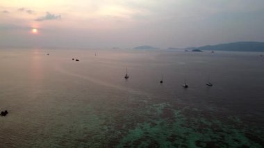 Sağ İHA 'ya dön. Günbatımında geleneksel uzun kuyruklu teknelerin bulunduğu tropikal bir sahil manzarası huzurlu ve resimli bir atmosfer yaratıyor.
