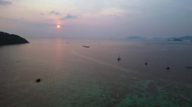 Panorama insansız hava aracı. Günbatımında geleneksel uzun kuyruklu teknelerin bulunduğu tropikal bir sahil manzarası huzurlu ve resimli bir atmosfer yaratıyor.