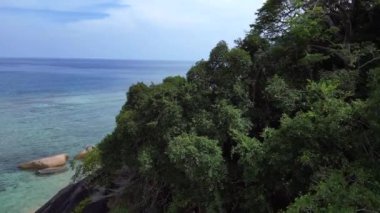 Üstten kumandalı hava aracı. Turkuaz su granit kayalar ve yemyeşil tropikal bitki örtüsüyle çevrili kumlu bir sahili nazikçe yıkıyor.
