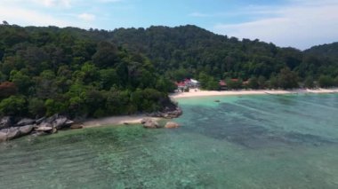 İHA 'yı getirin. Turkuaz okyanus suyu, tropik bir adada yemyeşil bir ormanı olan kayalık bir sahille buluşuyor.