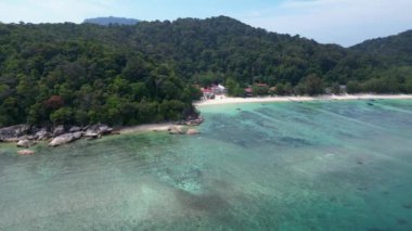 Panorama insansız hava aracı. Turkuaz okyanus suyu, tropik bir adada yemyeşil bir ormanı olan kayalık bir sahille buluşuyor.