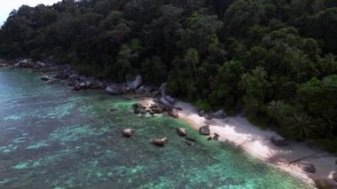 Geri geri uçun. Turkuaz su granit kayalar ve yemyeşil tropikal bitki örtüsüyle çevrili kumlu bir sahili nazikçe yıkıyor.