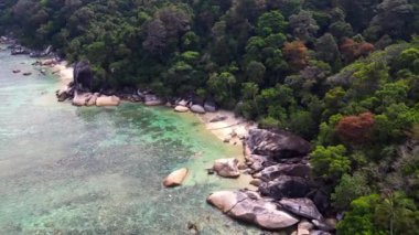 İHA 'lar yukarıdan aşağıya bakıyor. Turkuaz su granit kayalar ve yemyeşil tropikal bitki örtüsüyle çevrili kumlu bir sahili nazikçe yıkıyor.