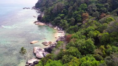 Panorama insansız hava aracı. Turkuaz su granit kayalar ve yemyeşil tropikal bitki örtüsüyle çevrili kumlu bir sahili nazikçe yıkıyor.