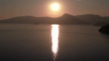 Bereketli yeşil tropikal ada gündoğumunda sakin okyanusla buluşuyor ve arka planda uzak dağlar var. panorama genel görünüm dronu 
