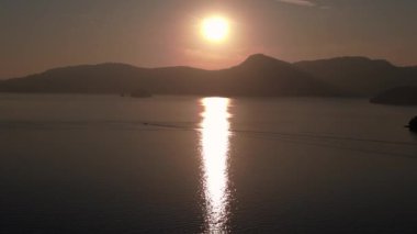 Bereketli yeşil tropikal ada gündoğumunda sakin okyanusla buluşuyor ve arka planda uzak dağlar var. panorama genel görünüm dronu 