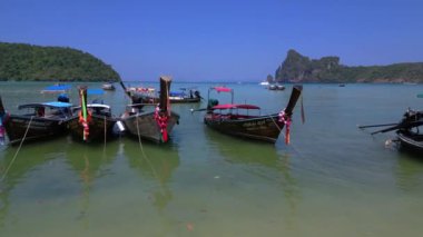 Tayland 'da tropik bir adanın yakınında sakin turkuaz sularda yüzen renkli geleneksel uzun kuyruklu tekneler var. uçuş üstü insansız hava aracı 