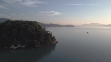 Bereketli yeşil tropikal ada gündoğumunda sakin okyanusla buluşuyor ve arka planda uzak dağlar var. panorama genel görünüm dronu 