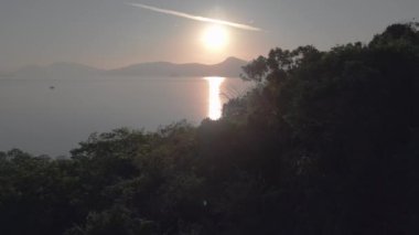 Bereketli yeşil tropikal ada gündoğumunda sakin okyanusla buluşuyor ve arka planda uzak dağlar var. uçuş üstü insansız hava aracı 