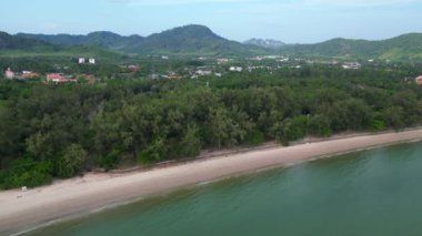 Turkuaz deniz, tropik bir plajı kumda yürüyen turistlerle yıkıyor ve arka planda yeşil tepeler var. uçuş üstü insansız hava aracı 