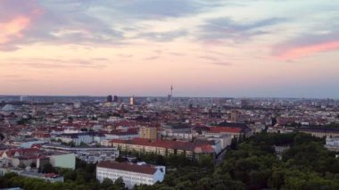 Güneş, Berlin şehrinin üzerinde batıyor. Binalara, Funkturm Kulesi 'ne ve aşağıdaki sokaklara sıcak bir ışıltı saçıyor. panorama genel görünüm dronu 