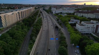 Berlin 'de gün batımında bir tren ve arabalarla geçen bir otobanın görüntüsü. İHA alçalıyor 