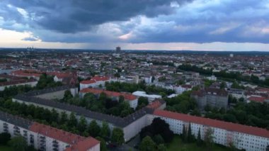 Günbatımında bulutlu bir gökyüzünün altında konut binaları, bir otoyol ve yemyeşil alanlar ile modern Avrupa şehir manzarası. Ters İHA uçuşu 