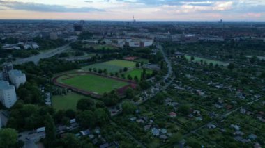 Yoğun kentsel manzarayla çevrili yeşil spor sahalarının hava görüntüsü batan güneşin sahne üzerine sıcak bir parıltı saçıyor. panorama genel görünüm dronu 