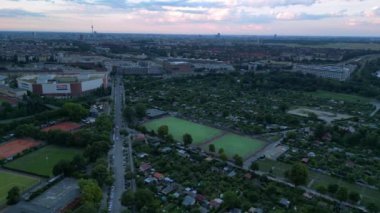 Yoğun kentsel manzarayla çevrili yeşil spor sahalarının hava görüntüsü batan güneşin sahne üzerine sıcak bir parıltı saçıyor. panorama genel görünüm dronu 