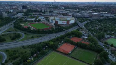 Yoğun kentsel manzarayla çevrili yeşil spor sahalarının hava görüntüsü batan güneşin sahne üzerine sıcak bir parıltı saçıyor. İHA 'yı eğ 