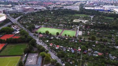 Yoğun kentsel manzarayla çevrili yeşil spor sahalarının hava görüntüsü batan güneşin sahne üzerine sıcak bir parıltı saçıyor. panorama yörünge dronu 