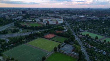 Yoğun kentsel manzarayla çevrili yeşil spor sahalarının hava görüntüsü batan güneşin sahne üzerine sıcak bir parıltı saçıyor. Ters İHA uçuşu 
