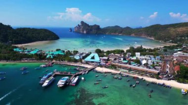 Phi phi Adası Tonsai rıhtımında turkuvaz suya yanaşmış tekneler ve güneşli bir günde Tayland 'da yürüyen turistler. Yukarıdan insansız hava aracı görüntüleri 