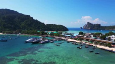 Phi phi Adası Tonsai rıhtımında turkuvaz suya yanaşmış tekneler ve güneşli bir günde Tayland 'da yürüyen turistler. uçuş üstü insansız hava aracı 