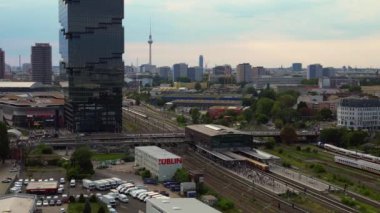 Berlin Warschauer istasyonu, birden fazla tren yolu, modern gökdelenler ve arka planda ikonik televizyon kulesi. Yukarıdan insansız hava aracı görüntüleri 