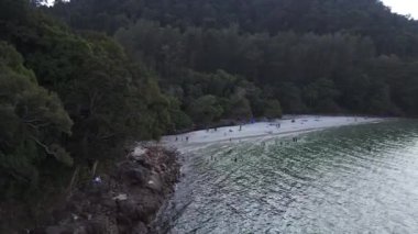 Turistler, Malezya 'daki yemyeşil tropikal ormanlarla kumlu kafatası sahillerinde dinleniyorlar. panorama genel görünüm dronu 