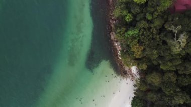 Turistler, Malezya 'daki yemyeşil tropikal ormanlarla kumlu kafatası sahillerinde dinleniyorlar. İHA kamerası aşağıya bakıyor 
