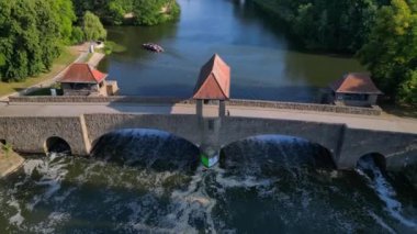 Palmengartenwehr Elster Weir, parlak bir yaz gününde yemyeşil ağaçlarla çevrili bir köprünün altından akan nehrin havadan görünüşü. hız rampası hiper hareket zaman aşımı 