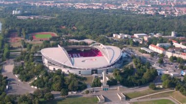 Güneşli bir yaz gününde Rb Leipzig 'e ev sahipliği yapan bir arenanın hava manzarası yemyeşil çevreyi ve şehir manzarasını gözler önüne seriyor. panorama genel görünüm dronu 