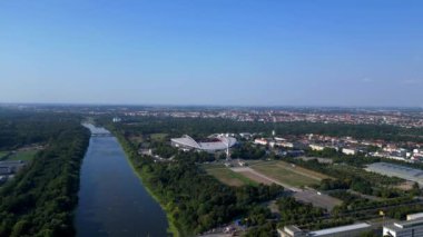 Güneşli bir yaz gününde Rb Leipzig 'e ev sahipliği yapan bir arenanın hava manzarası yemyeşil çevreyi ve şehir manzarasını gözler önüne seriyor. panorama genel görünüm dronu 